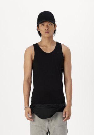 Top sin mangas negro hecho de una tela transpirable, combinado con una riñonera negra llevada en la cintura sobre pantalones cargo gris claro.