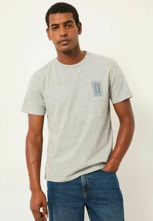 Gray cotton T-shirt with short sleeves, round neck, and a blue graphic pocket detail. Model wears blue jeans. Smooth texture.