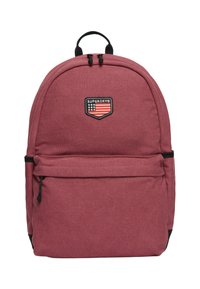 Mochila de tela roja con un diseño redondeado, que cuenta con un bolsillo frontal con cremallera y un parche con el logo. Detalles en negro en la cremallera y las correas.