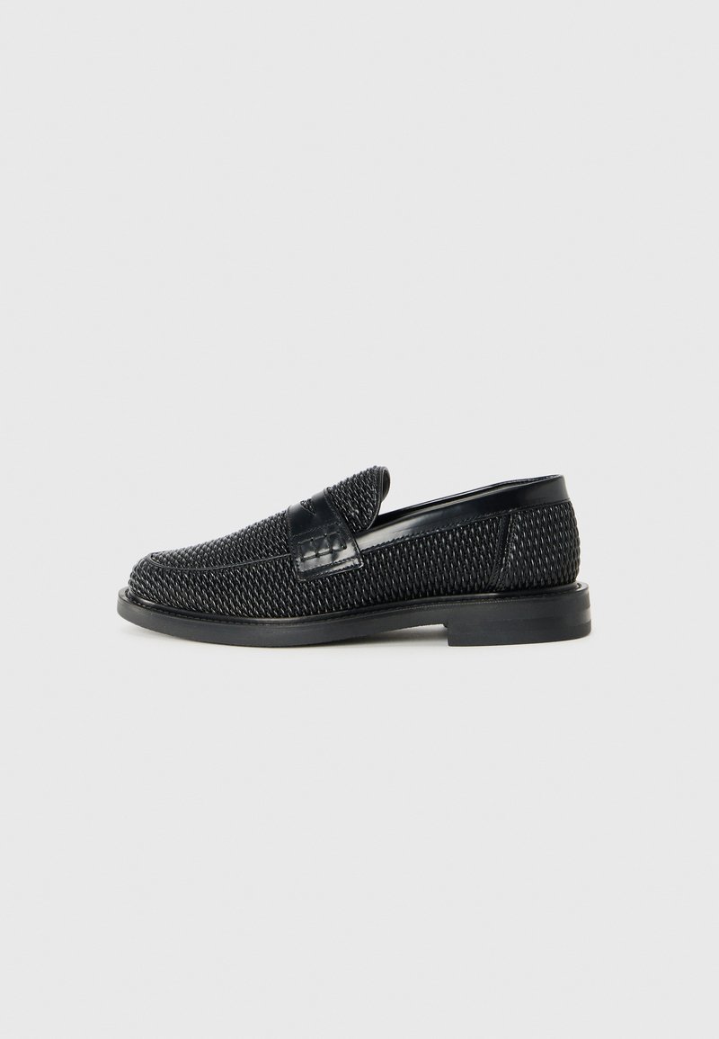 Schwarzer geflochtener Slipper mit einem glatten Lederakzent im Obermaterial, einem runden Zehendesign und einer flachen Gummisohle.