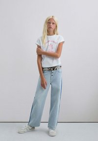 Witte katoenen t-shirt met roze print, gecombineerd met lichtblauwe wijde jeans met blauwe zijkanten, en witte sneakers.