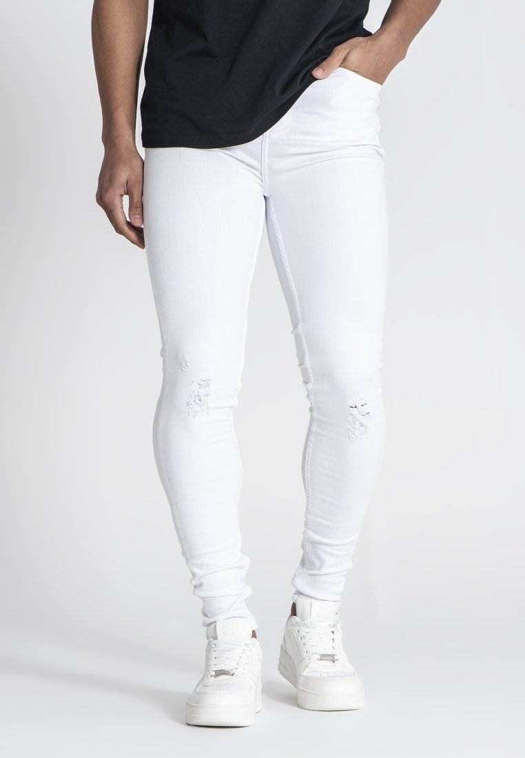 Jeans de denim blanco elástico con un corte slim, presentando detalles desgastados y combinados con zapatillas blancas. Camiseta negra metida en la cintura.