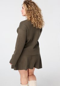 Olijfgroene gebreide jurk met een aangesloten lijfje en een uitlopende rok. Lange mouwen, gestructureerde stof en een ronde hals.
