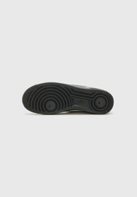 Black rubber sneaker sole with a textured surface, circular grips, and ridges; features logo embossed on the midsole for grip enhancement.