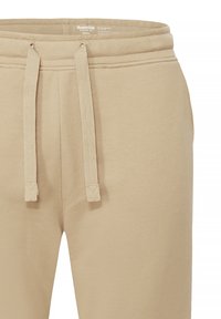 Beige Sweatpants mit Kordelzugbund, aus weichem Fleece-Material, mit seitlichen Taschen und glatter Oberfläche.