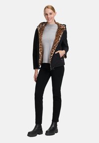 Czarna kurtka z brązowym podszewkowym wzorem w panterę, szary sweter, czarne spodnie i czarne botki za kostkę. Posiada kaptur i zamek błyskawiczny z przodu.