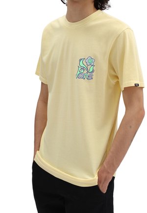 Żółta bawełniana koszulka z krótkim rękawem, z graficznym wzorem na lewej piersi, zawierająca elementy kwiatowe i tekstowe.