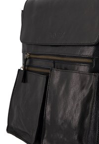 Schwarze Ledertasche mit Klappe, ausgestattet mit zwei vorderen Reißverschlusstaschen und sichtbaren Nähten. Strukturierte Oberfläche mit einem dezenten Glanz.