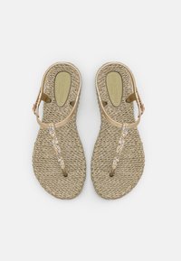 Sandali beige con texture intrecciata, dotati di una fascia dorata lucida decorata con strass trasparenti. Include una fibbia regolabile alla caviglia.