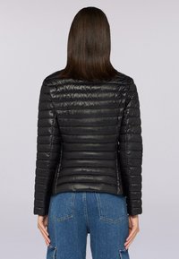 Giubbotto invernale nero con cuciture orizzontali. Tessuto liscio e lucido. Design aderente, lunghezza leggermente accorciata e due tasche laterali.