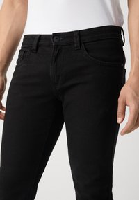 Jeans de mezclilla negra con una forma ajustada, que cuentan con un cierre de botón, bolsillos frontales y detalles de costura sutiles. Textura suave y diseño limpio.