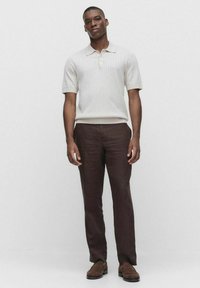 Ljusbeige ribbad polo med kort ärm, kombinerad med mörkbruna linnbyxor och bruna skor. Neutral, strukturerad tyg.