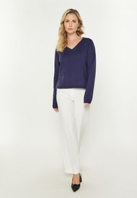 Pulover bleumarin cu decolteu în V din material moale, asortat cu pantaloni albi cu picioare largi și pantofi negri cu toc pătrat. Design simplu, ajustat, cu mâneci lungi.