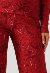 Leggings à motifs floraux rouges en tissu doux et extensible avec de grandes pétales superposées et un léger éclat. Mains reposant sur les hanches.
