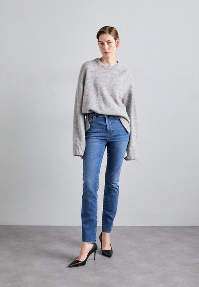 Gray oversized sweater with ribbed cuffs, paired with blue high-waisted skinny jeans, and black pointy-toed high heels. Smooth textures.