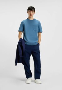 T-shirt azzurro chiaro a maniche corte con taschino sul petto, abbinato a pantaloni cargo blu scuro con tasche e sneakers bianche.