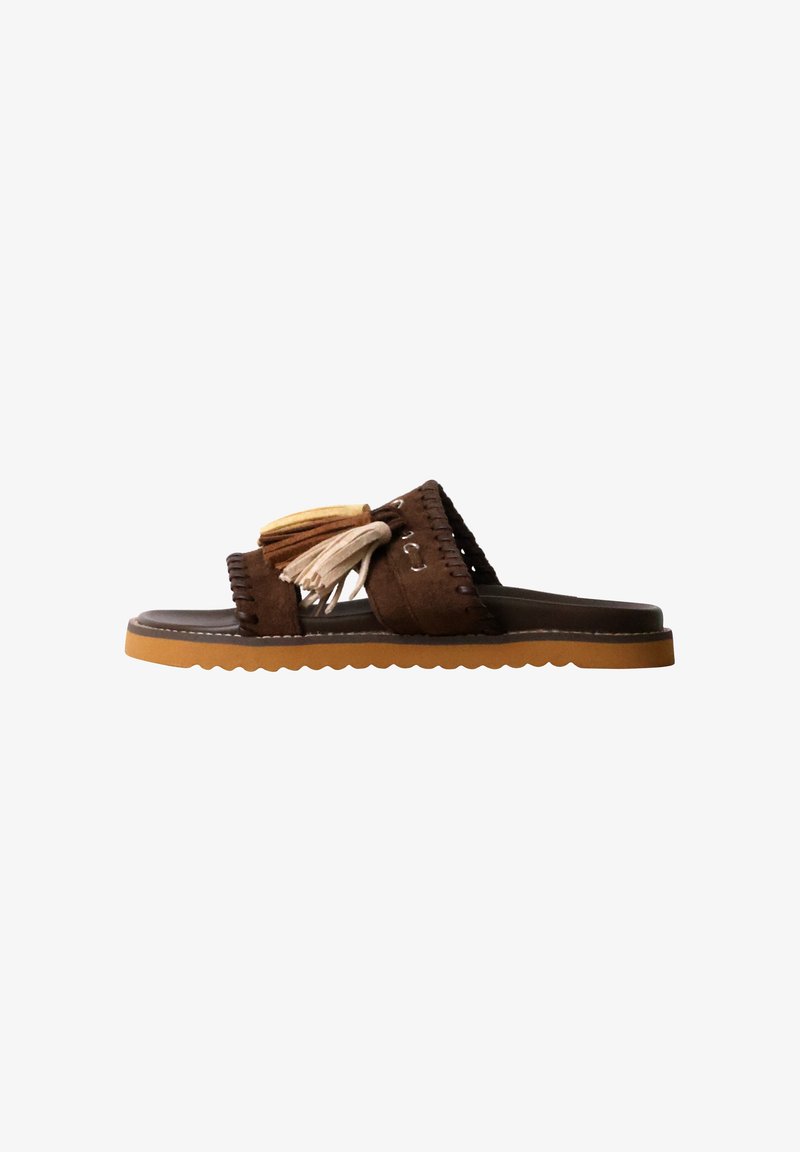 Sandale mule en daim marron avec deux pampilles décoratives beige et marron clair sur la bride et une semelle en caoutchouc marron clair aux bords ondulés.