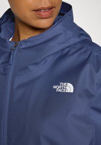 Navy blue jacket with a zipper and hood. Made from textured fabric featuring a white logo on the left chest.