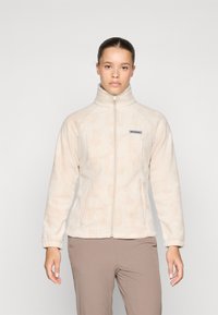 Chaqueta de forro polar beige con cuello alto, cierre de cremallera y un sutil patrón texturizado. Presenta mangas raglán y un logo en el lado izquierdo del pecho.