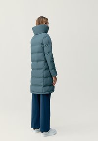 Tealfärgad puffjacka med hög krage, med en stickad design och långa ärmar, kombinerad med vida marinblå byxor och vita sneakers.