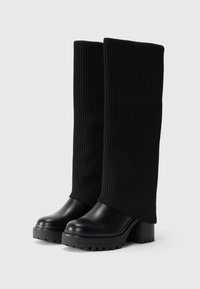Black ankle boots featuring a ribbed knitted upper and smooth leather toe. Chunky platform sole with textured grip.