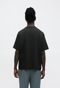 Μαύρο κοντομάνικο T-shirt με χαλαρή εφαρμογή, διαθέτοντας στρογγυλή λαιμόκοψη και ομαλή υφή, φαίνεται από πίσω.