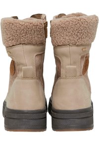 Bottes en suède beige avec un col duveteux beige, fermeture éclair sur le côté, semelle en caoutchouc texturée et une étiquette de logo marron à l'arrière.