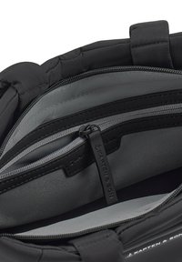 Svart ryggsäck med ett slätt grått foder, som visar ett blixtlåsförsett fack och en sydd logotypetikett. Flera fack för organisering.