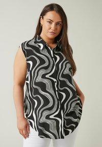 Blusa senza maniche a righe bianche e nere con chiusura a bottoni, caratterizzata da curve e onde morbide nel design. Realizzata in tessuto leggero.