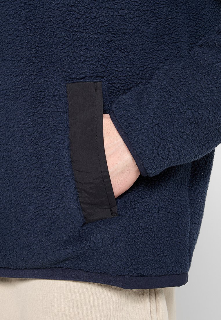 Pullover in pile di colore blu navy, con una superficie testurizzata e un bordo della tasca nero a contrasto. Tessuto morbido con una vestibilità comoda.