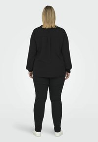 Černý svetr s kulatým výstřihem a měkkou, strukturovanou tkaninou. V kombinaci s černými slim-fit kalhotami a bílými teniskami, z pohledu zezadu.