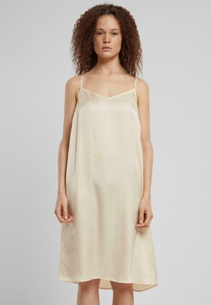 Robe slip en soie de couleur jaune pâle avec des fines bretelles, un décolleté en V et une forme évasée. Texture lisse avec un subtil éclat et un ourlet irrégulier.