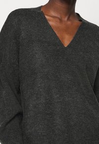 Dunkelgrauer Strickpullover mit V-Ausschnitt, der eine lockere Passform und eine weiche Textur aufweist. Deutliche subtile Farbvariationen sind sichtbar.