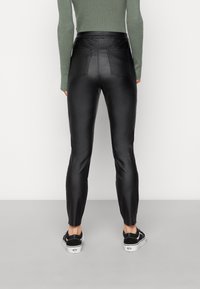 Leggings pretos em couro sintético com um design ajustado, cintura alta e dois bolsos traseiros, combinados com sapatilhas pretas de tela.