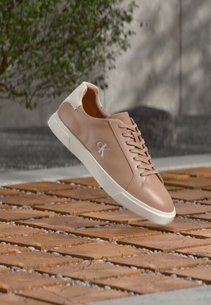 Sapatilha de couro cor de rosa claro com calcanhar branco. Apresenta atacadores planos, biqueira arredondada e um logótipo subtil na lateral. Sola texturada visível.