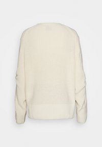 Roomkleurige gebreide trui met een losse pasvorm, geribbelde textuur en lange mouwen. De achterkant heeft een eenvoudig ontwerp met een horizontale naad ter hoogte van de taille.