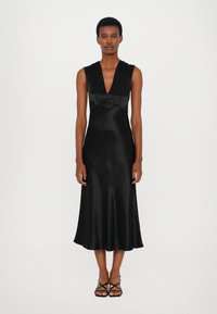 Rochie din satin negru cu decolteu adânc în V, design fără mâneci, corset ajustat și fustă fluentă. Model purtând sandale negre cu bretele.