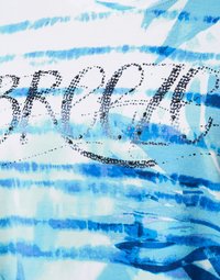 White fabric t-shirt featuring blue watercolor patterns and the word "BREEZY" in black sequined letters. Soft texture with smooth finish.