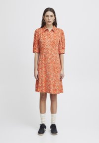 Abito a maniche corte con colletto di un brillante arancione con motivo floreale; silhouette a campana; abbinato a sneakers nere e calze color crema.
