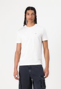 Witte katoenen T-shirt met een ronde halslijn en korte mouwen, met een klein geborduurd logo op de borst. Gecombineerd met donkere cargoshorts.