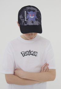 Cappello nero con un motivo tie-dye presenta un grafico di un personaggio Pokémon viola e il testo "Pokémon". T-shirt bianca che mostra il logo di Pokémon.