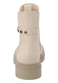 Botín de tobillo de polipiel beige con una textura suave, que presenta una correa y acentos de tachuelas metálicas. Suela gruesa con un diseño de patrón.