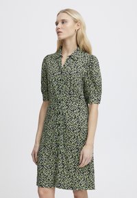 Abito nero a maniche corte con un motivo floreale in verde e bianco, chiusura a bottoni, design con colletto, vestibilità leggermente ampia, lunghezza al ginocchio.