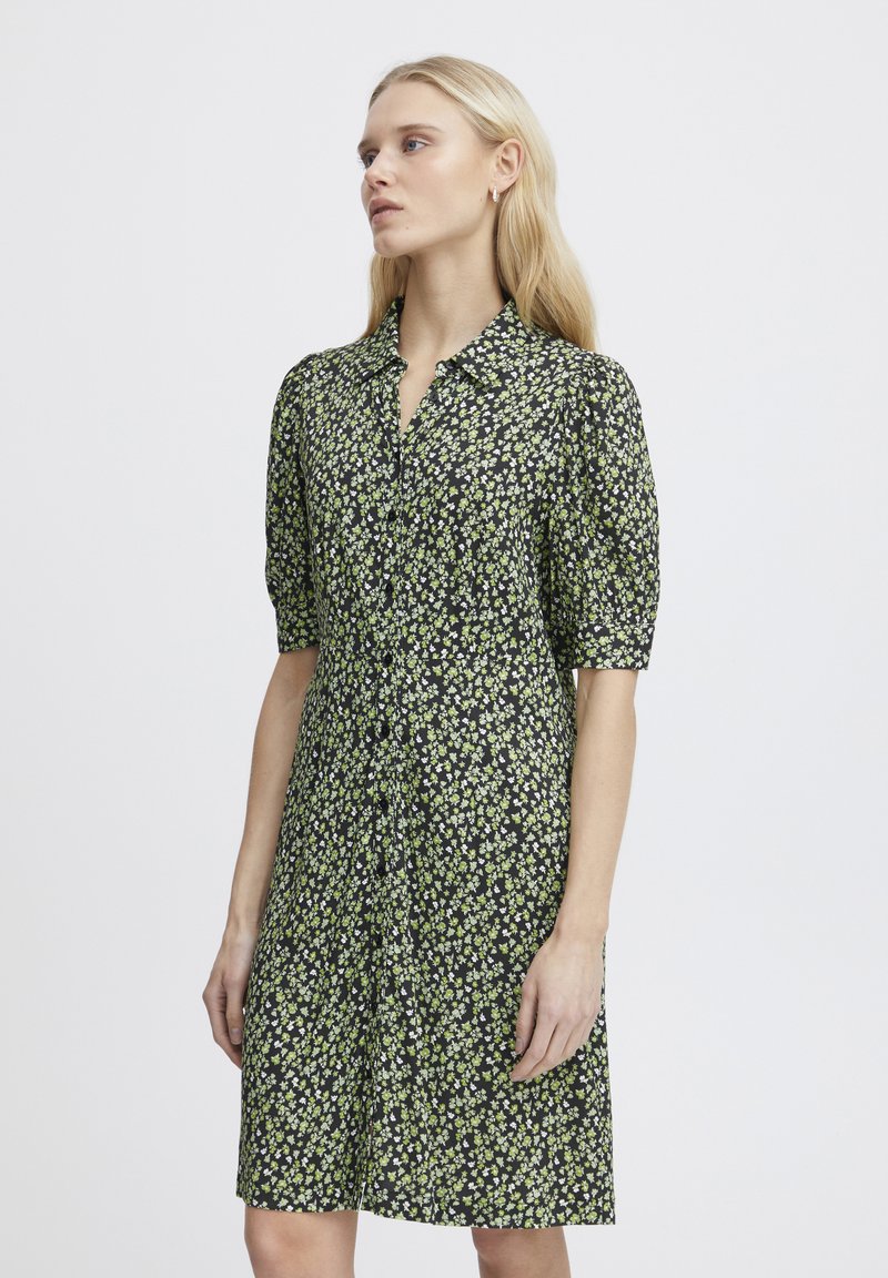 Abito nero a maniche corte con un motivo floreale in verde e bianco, chiusura a bottoni, design con colletto, vestibilità leggermente ampia, lunghezza al ginocchio.