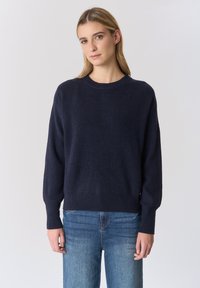 Maglione lavorato a maglia blu navy con scollo rotondo, maniche lunghe e trama a coste. Abbinate a jeans azzurri a gamba dritta.