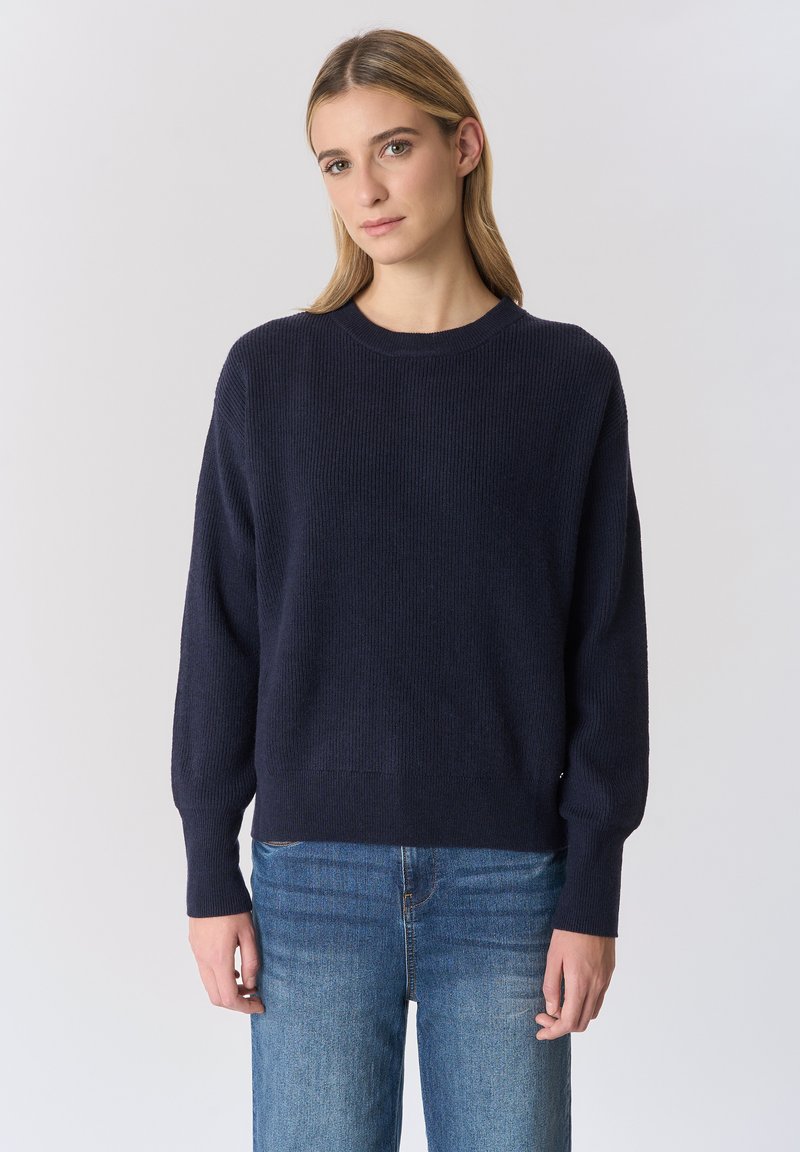 Maglione lavorato a maglia blu navy con scollo rotondo, maniche lunghe e trama a coste. Abbinate a jeans azzurri a gamba dritta.