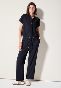 Marineblauwe jumpsuit met korte mouwen, knoopsluiting aan de voorkant en een taille met trekkoord. Kenmerkt zich door een textuurstof en een ontspannen wijde broekspijp ontwerp.