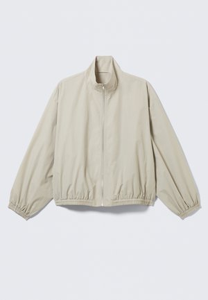 Veste zippée beige clair avec poignets et ourlet élastiques, col montant, présentée sur une surface plane.