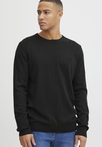 Maglione nero a maniche lunghe in un tessuto a maglia liscia con colletto rotondo e polsini a costine. Dettaglio del logo piccolo sul petto.