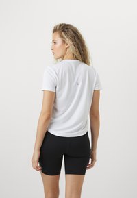 Camiseta blanca de manga corta, hecha de una tela suave, combinada con pantalones cortos negros de cintura alta; presenta un logo sutil en la parte posterior.